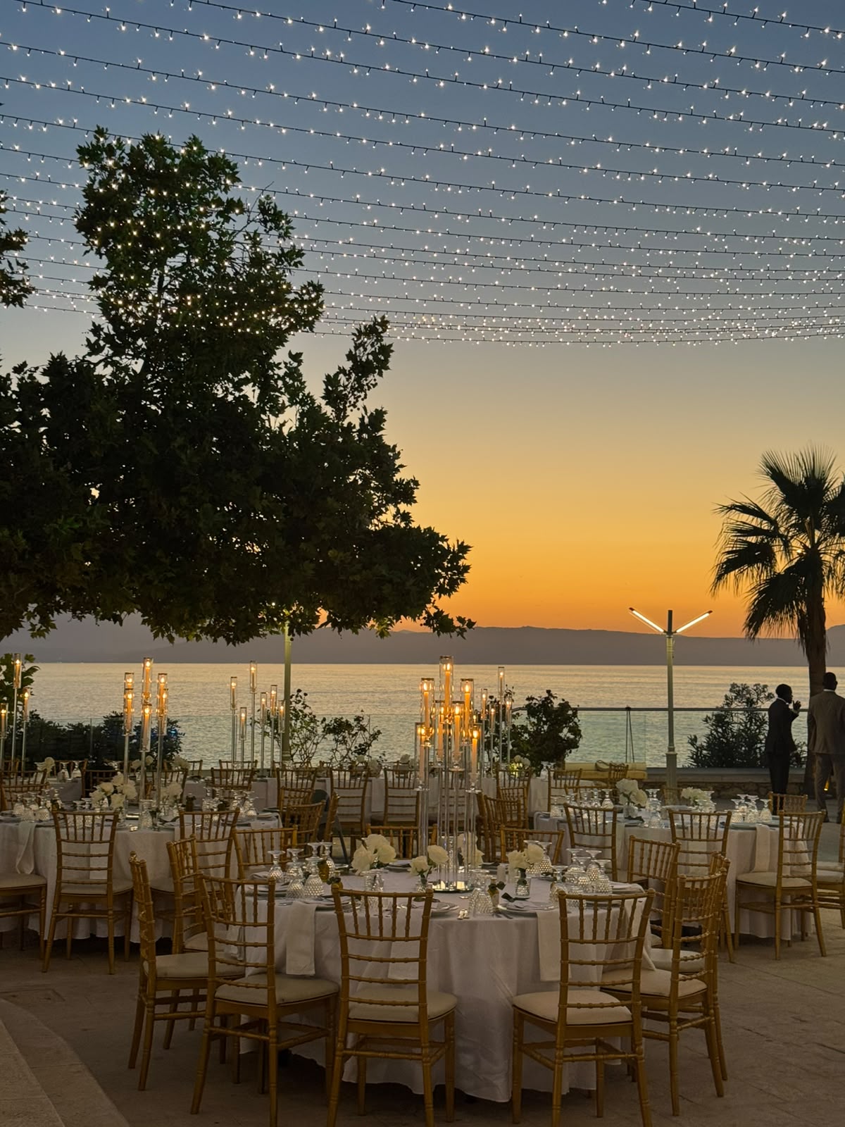 Tables set for dinner beneath trees overlooking the sea at Ktima Pavlaki